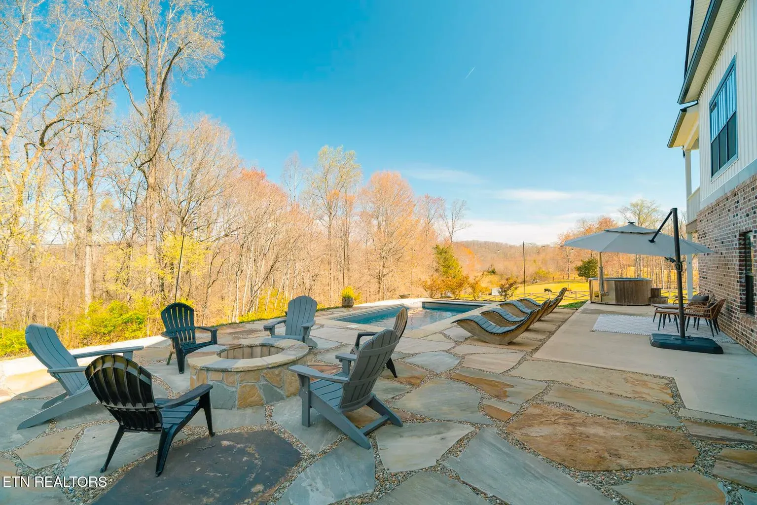 A patio with chairs , umbrellas and a fire pit in front of a house.