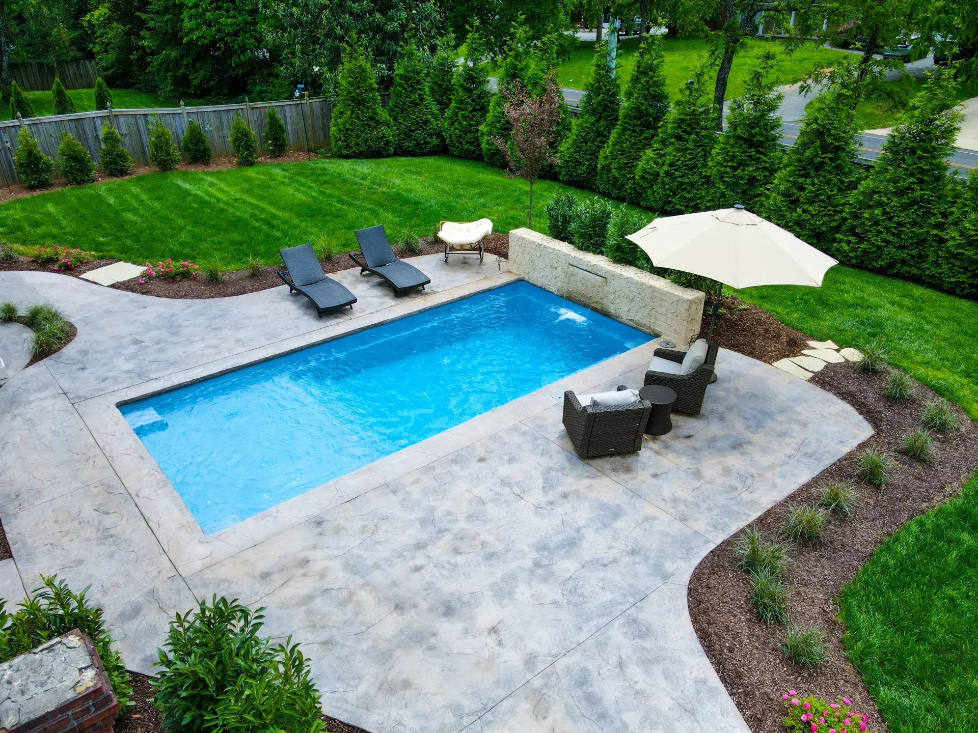 An aerial view of a swimming pool with chairs and umbrellas in a backyard.