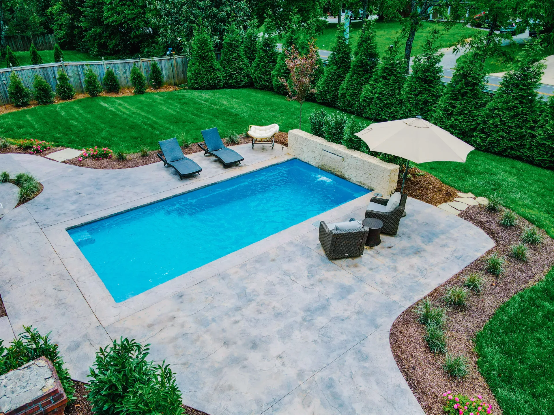 A custom built swimming pool installed by sunshine outdoor living pool builder surrounded by chairs and umbrellas at sunset.