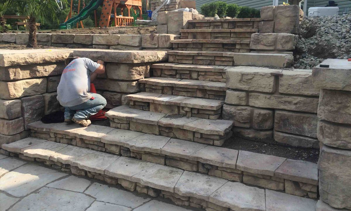 A man is kneeling down on a set of stone stairs.
