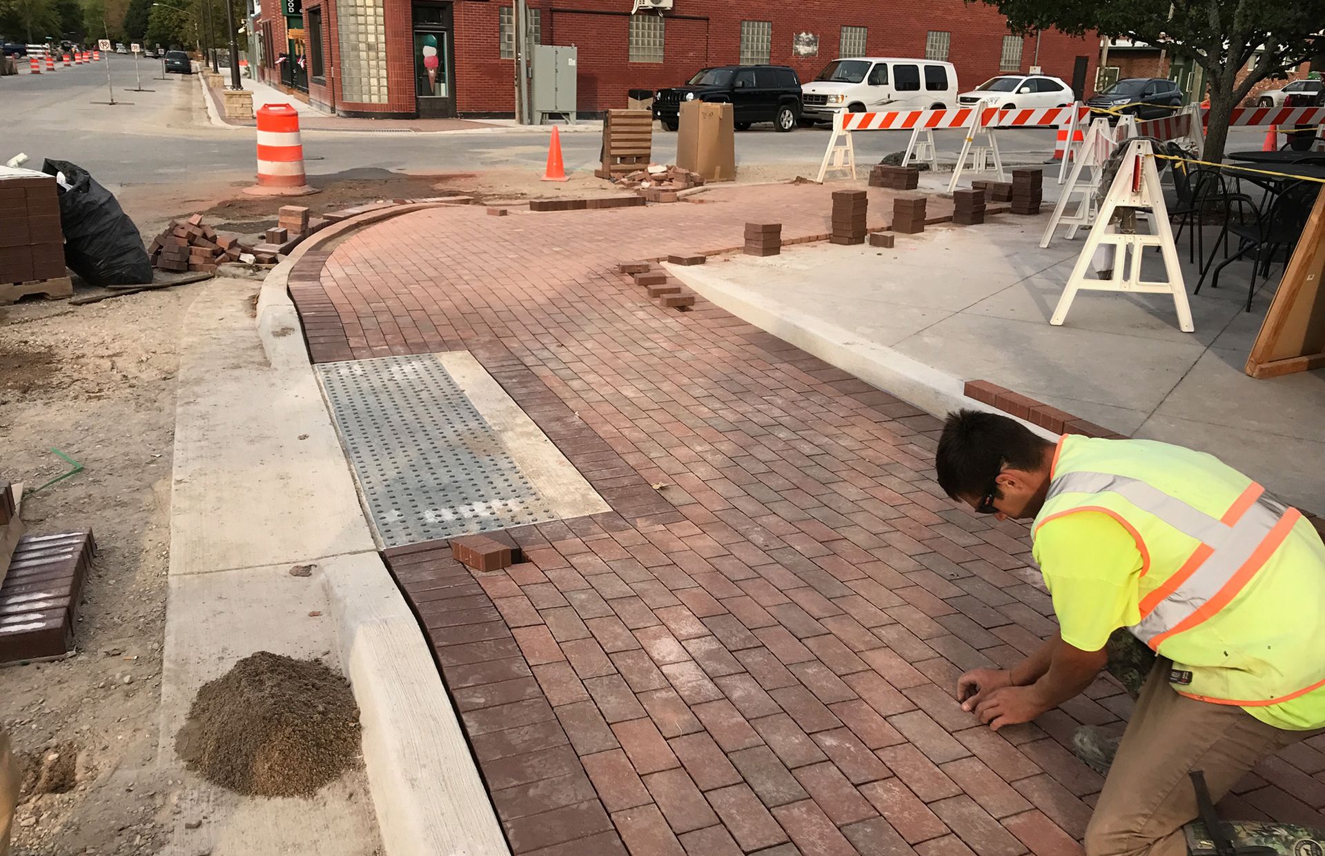 A man in a yellow vest is working on a brick sidewalk