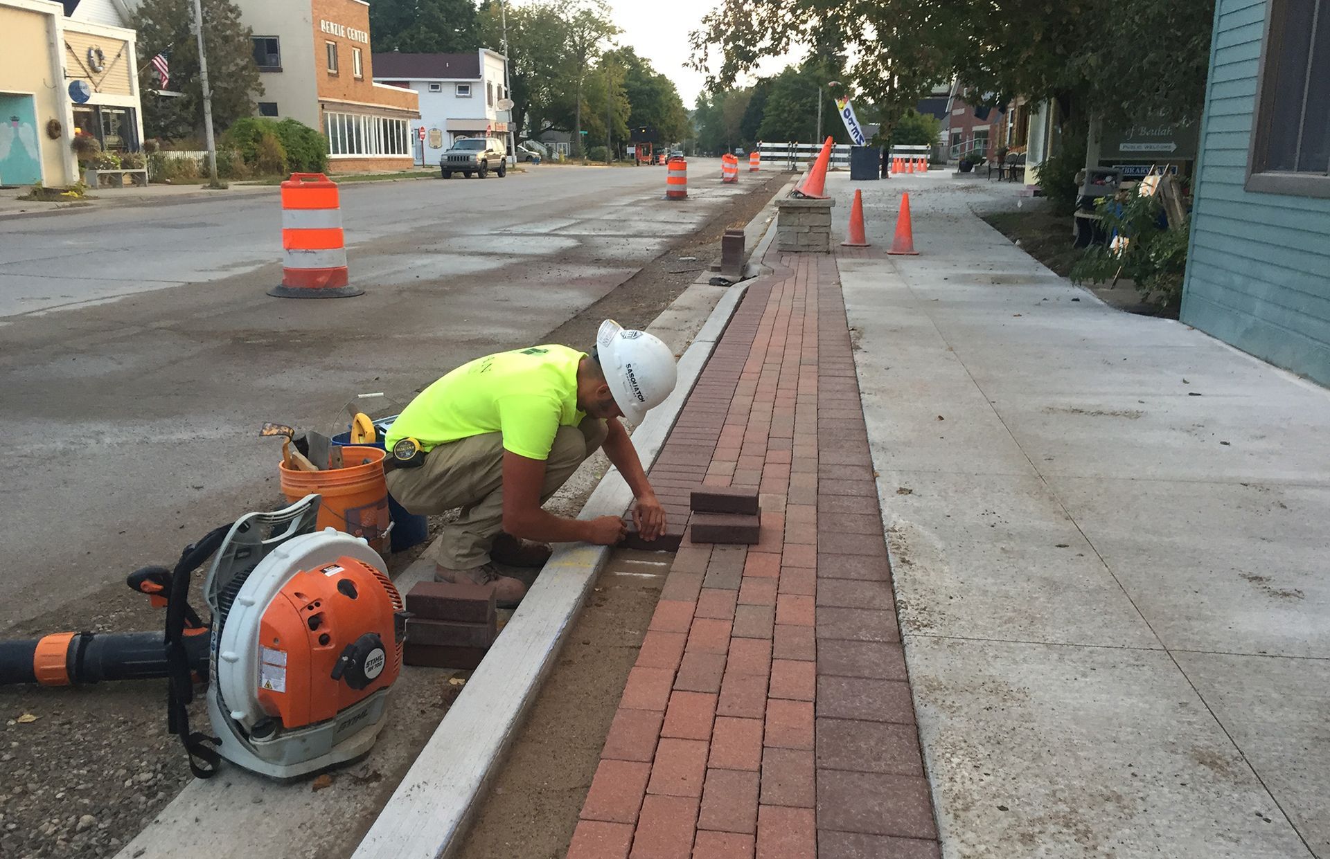 A construction worker is laying bricks on the sidewalk