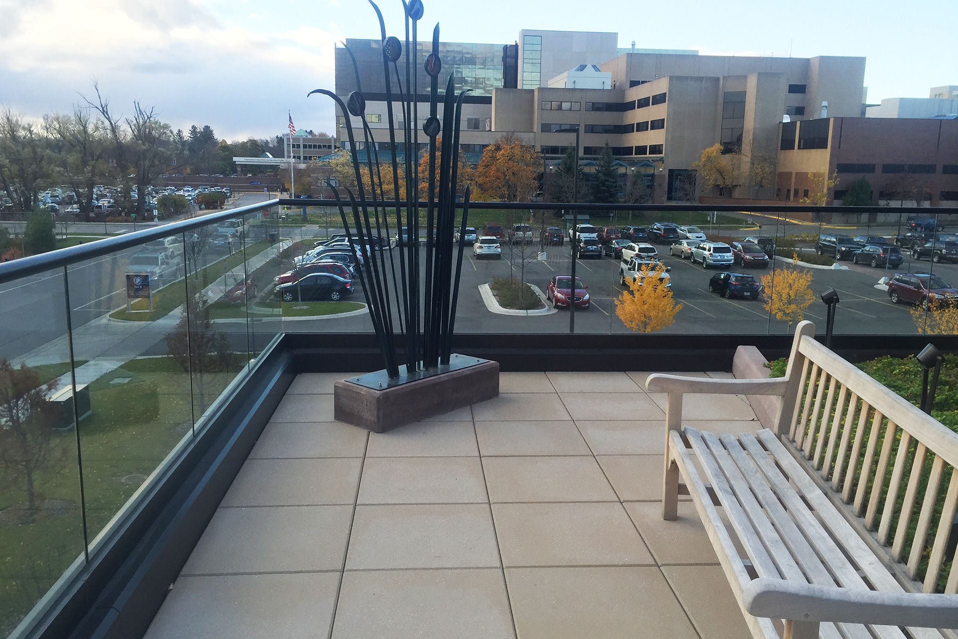 A white bench sits on a balcony overlooking a parking lot