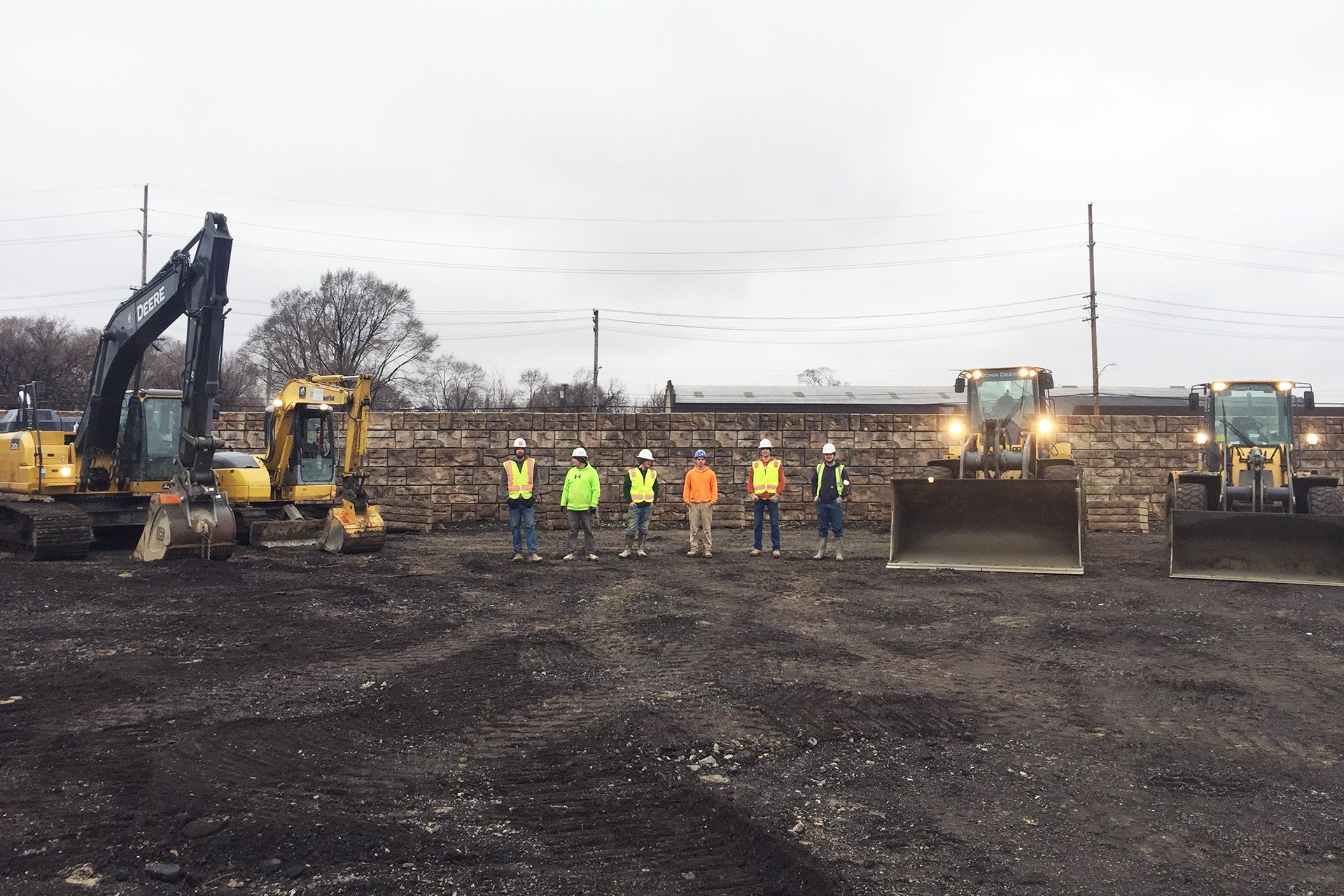 A group of construction workers are standing in a field with tractors.