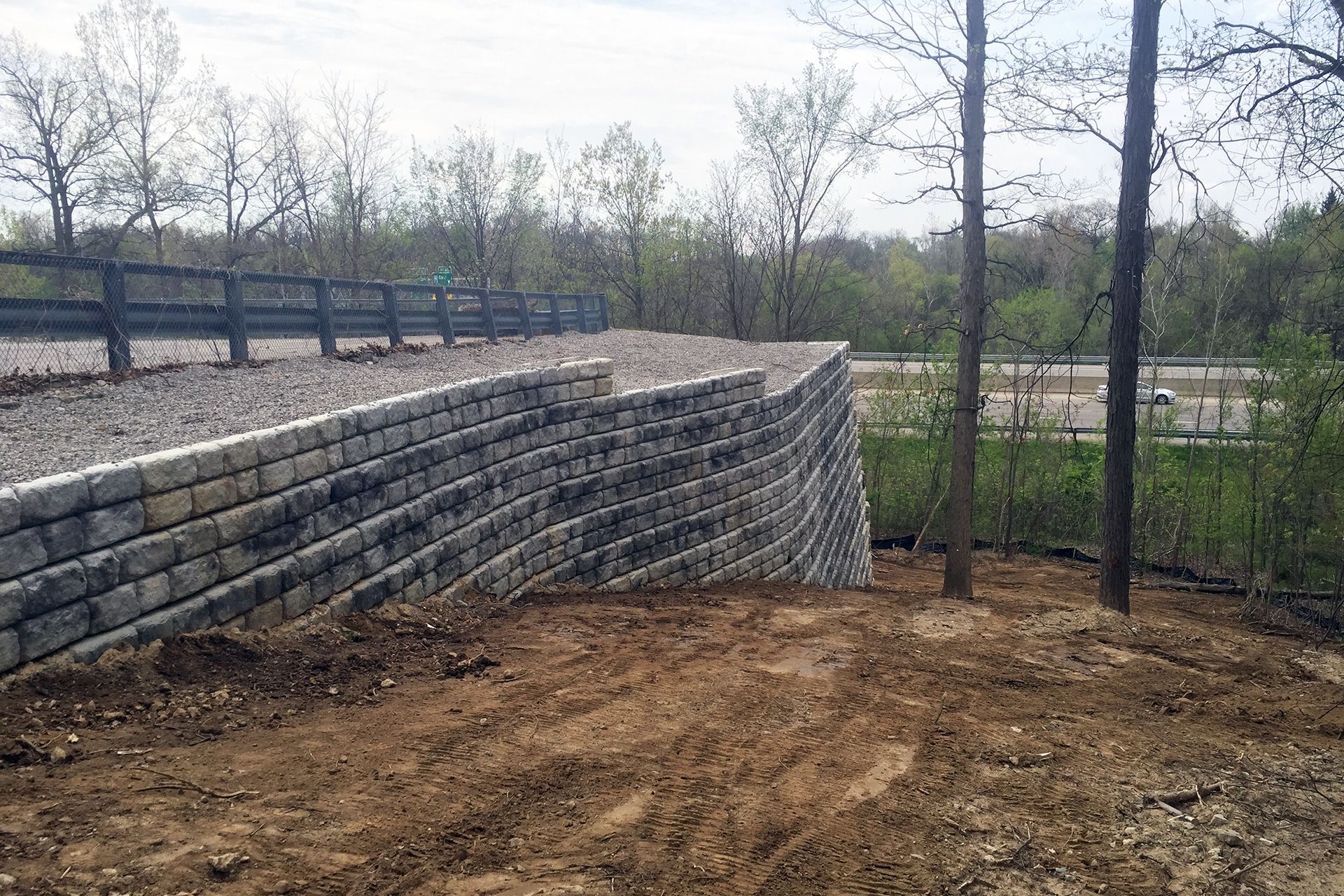 A large stone wall is sitting on top of a dirt hill surrounded by trees.