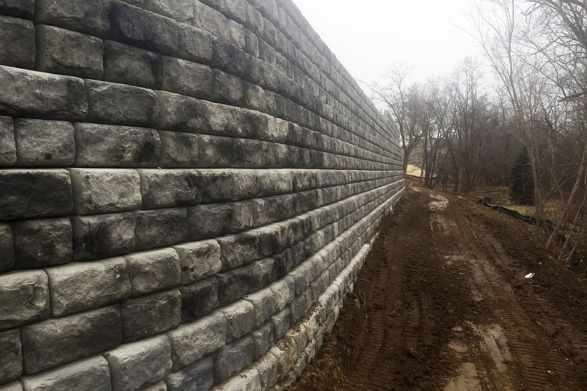 A large brick wall is along the side of a dirt road.