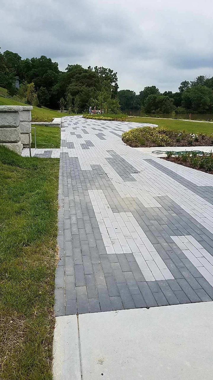 A brick walkway leading to a grassy field in a park.