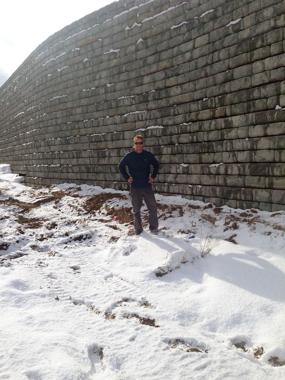 A man standing in the snow in front of a brick wall