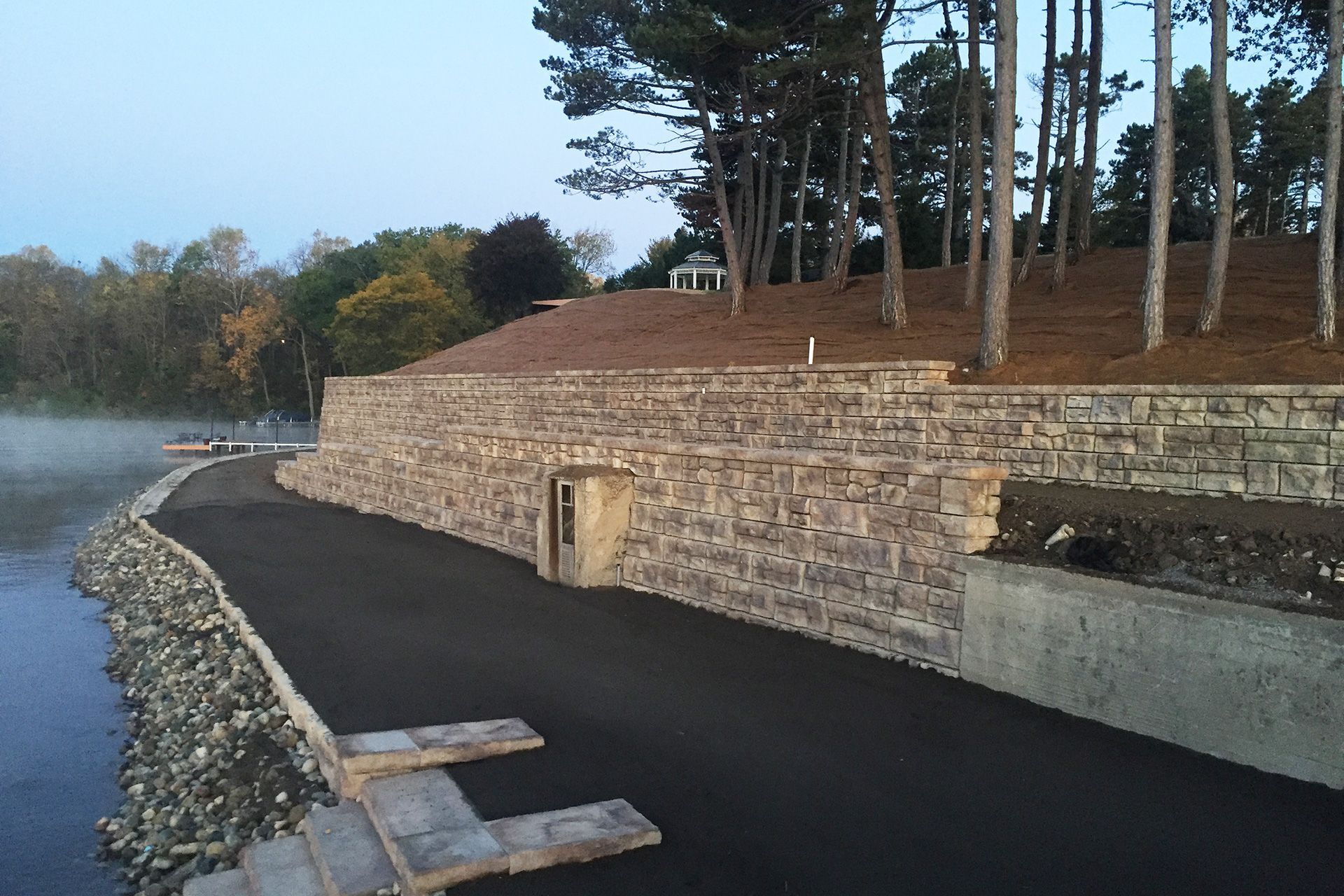 A stone wall along the side of a road next to a body of water