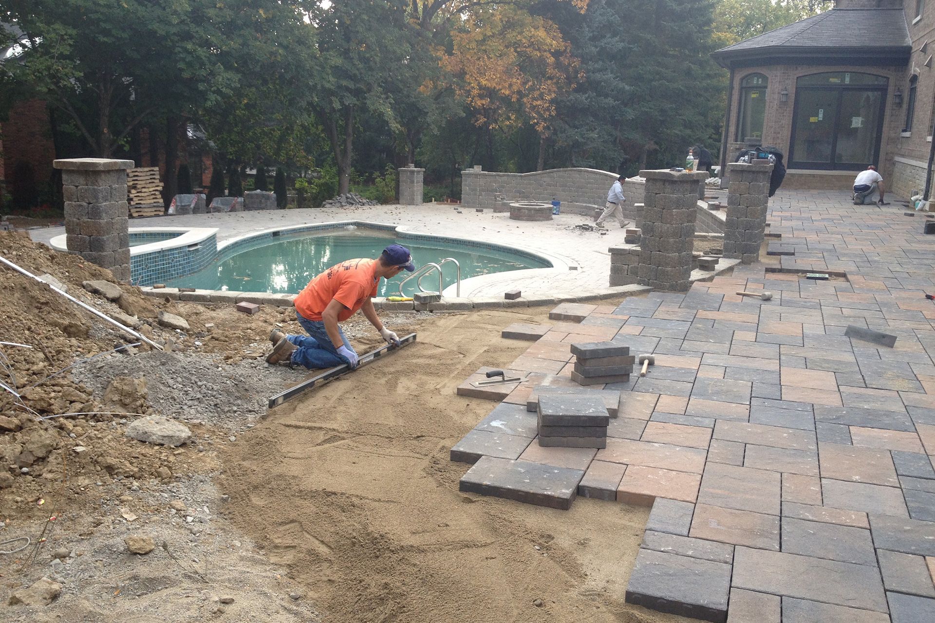 A man is working on a patio in front of a pool