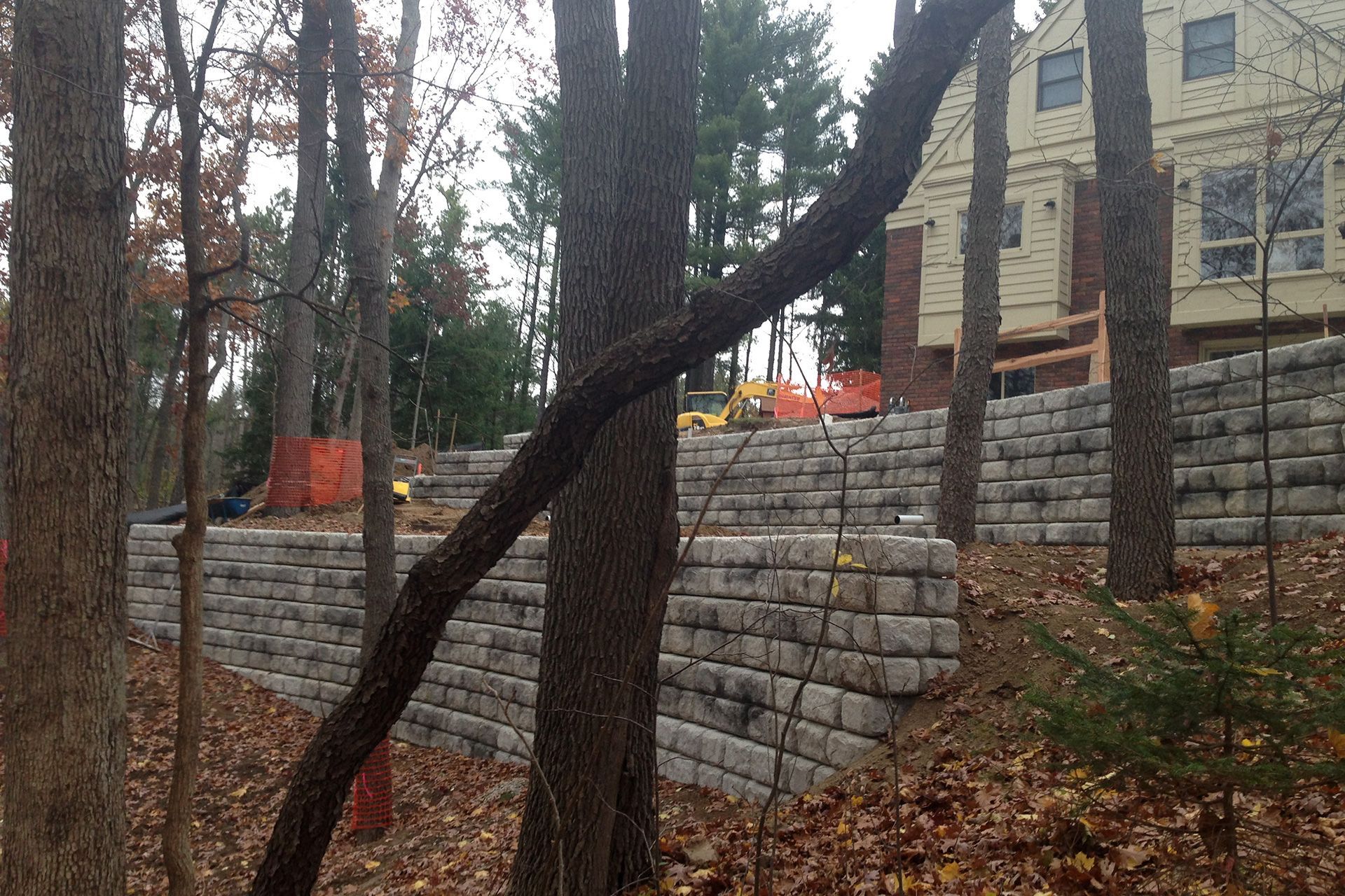 A brick wall is being built in the woods in front of a house