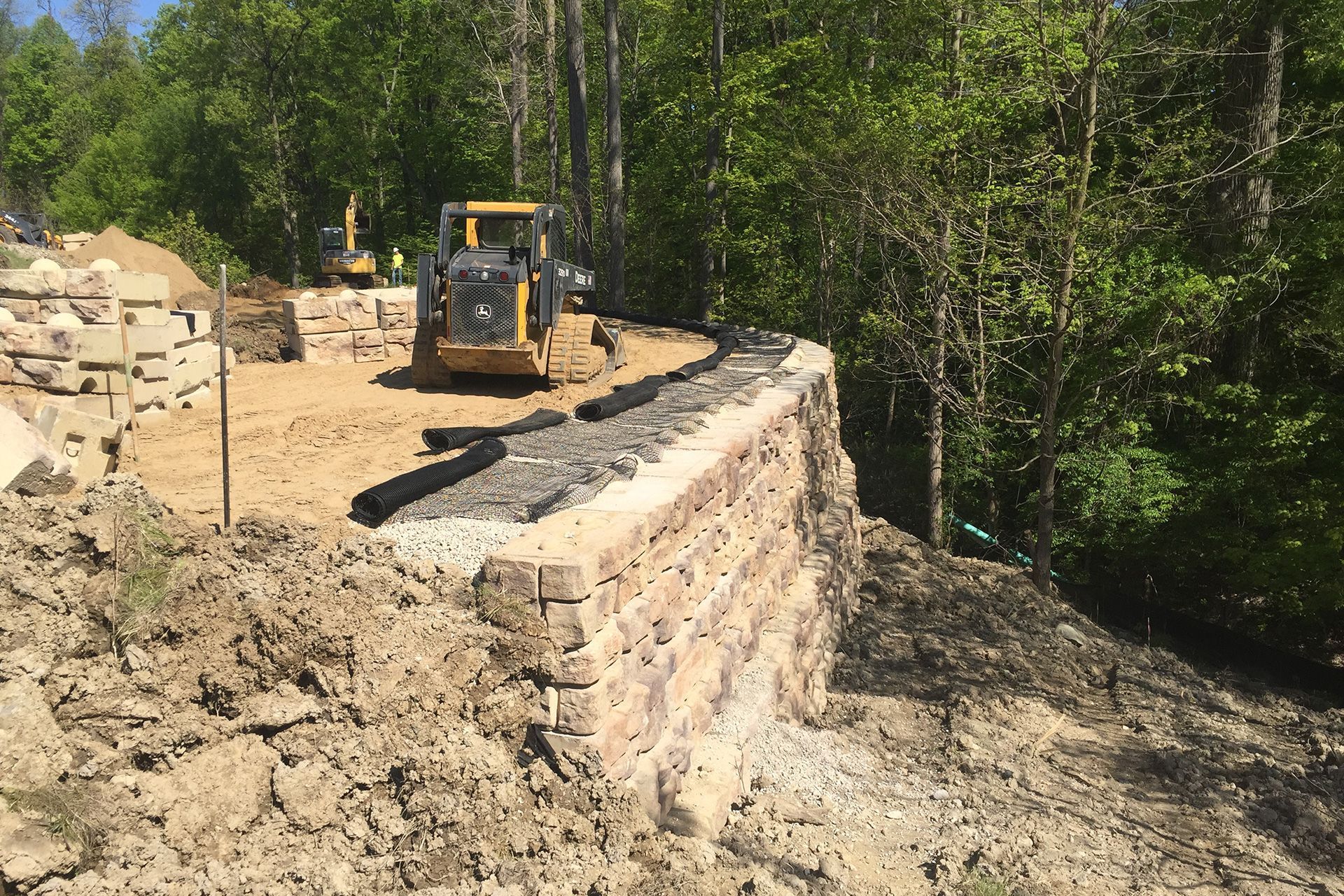 A bulldozer is working on a stone wall in the woods.