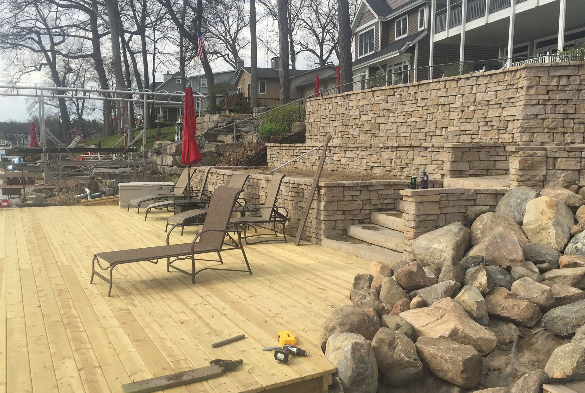 A wooden deck with lawn chairs and umbrellas on it next to a stone wall.