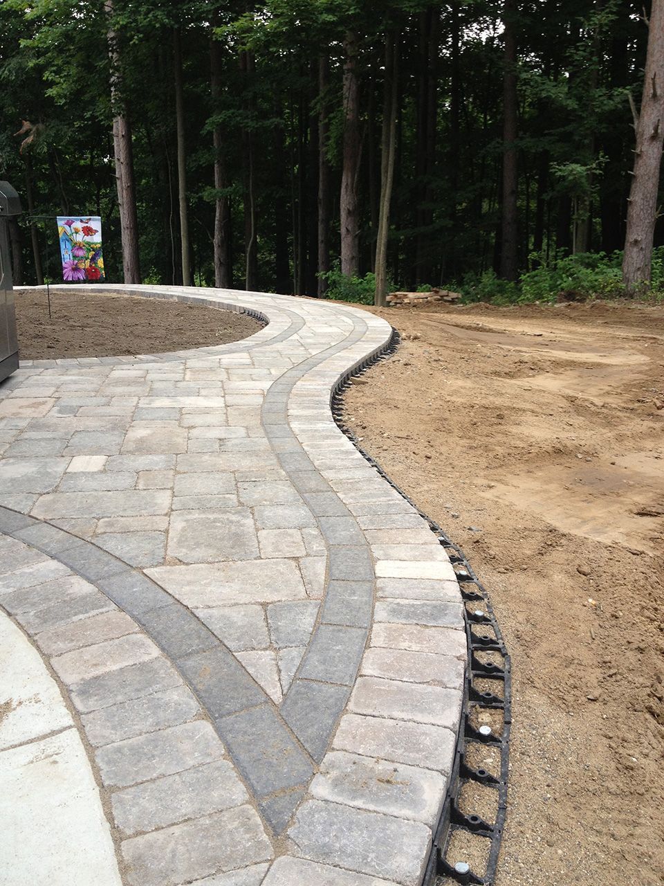 A brick walkway going through a dirt field with trees in the background