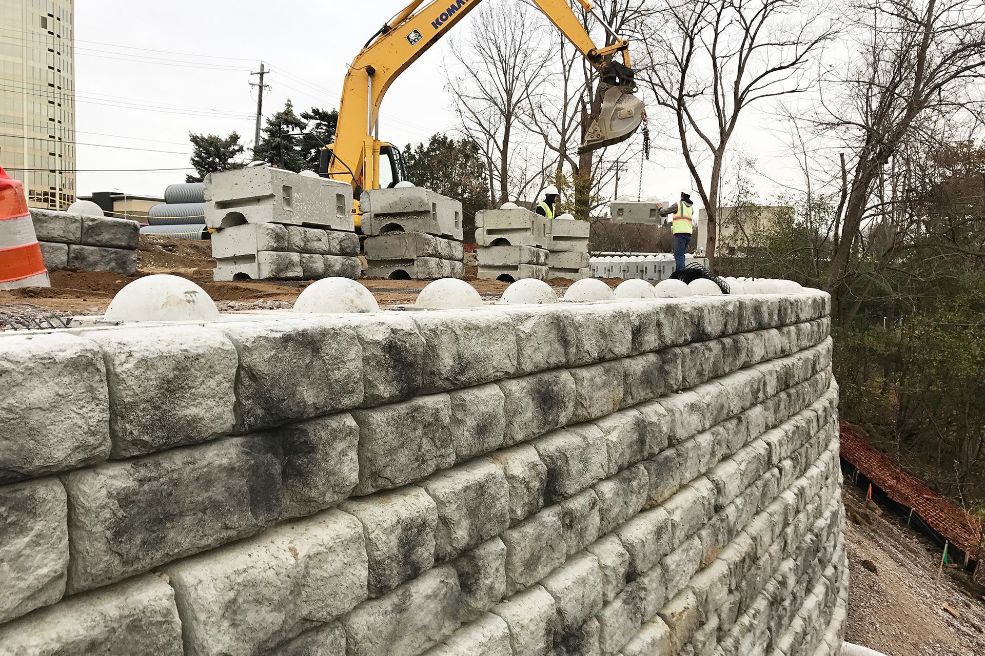 A large brick wall is being built with a yellow excavator in the background.