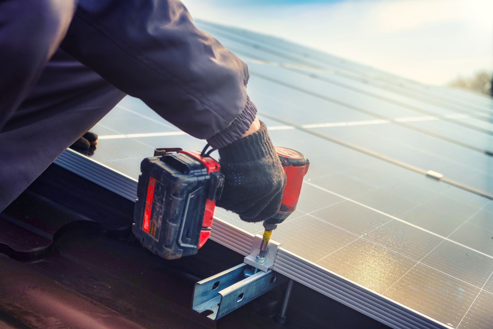Worker installing solar panel using a power drill on a rooftop under sunlight.