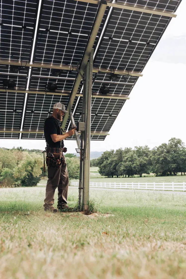 Man installing solar panels outdoors on a sunny day. He is working near a field.