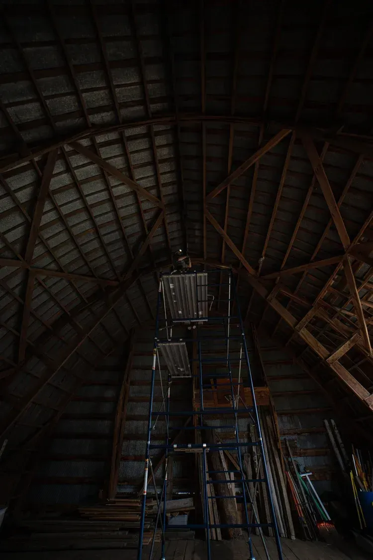 Interior of an attic with scaffolding, angled wood ceiling. Dim lighting.