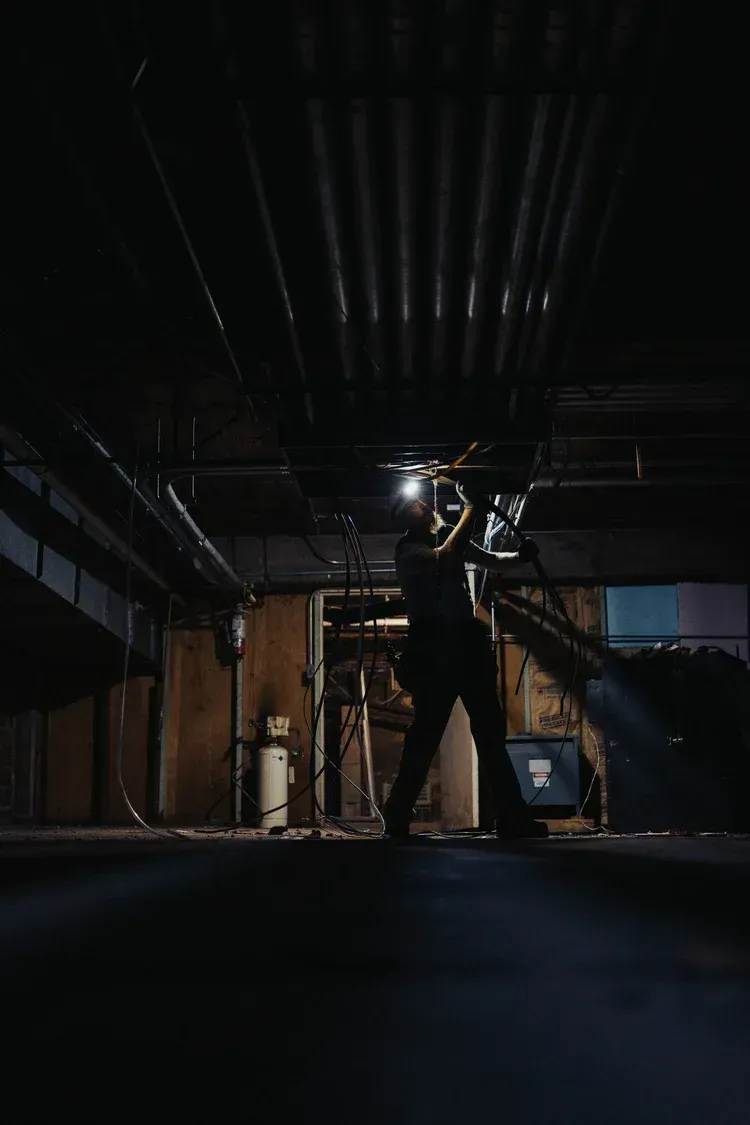 Person in dark room holding a flashlight, looking up at pipes.