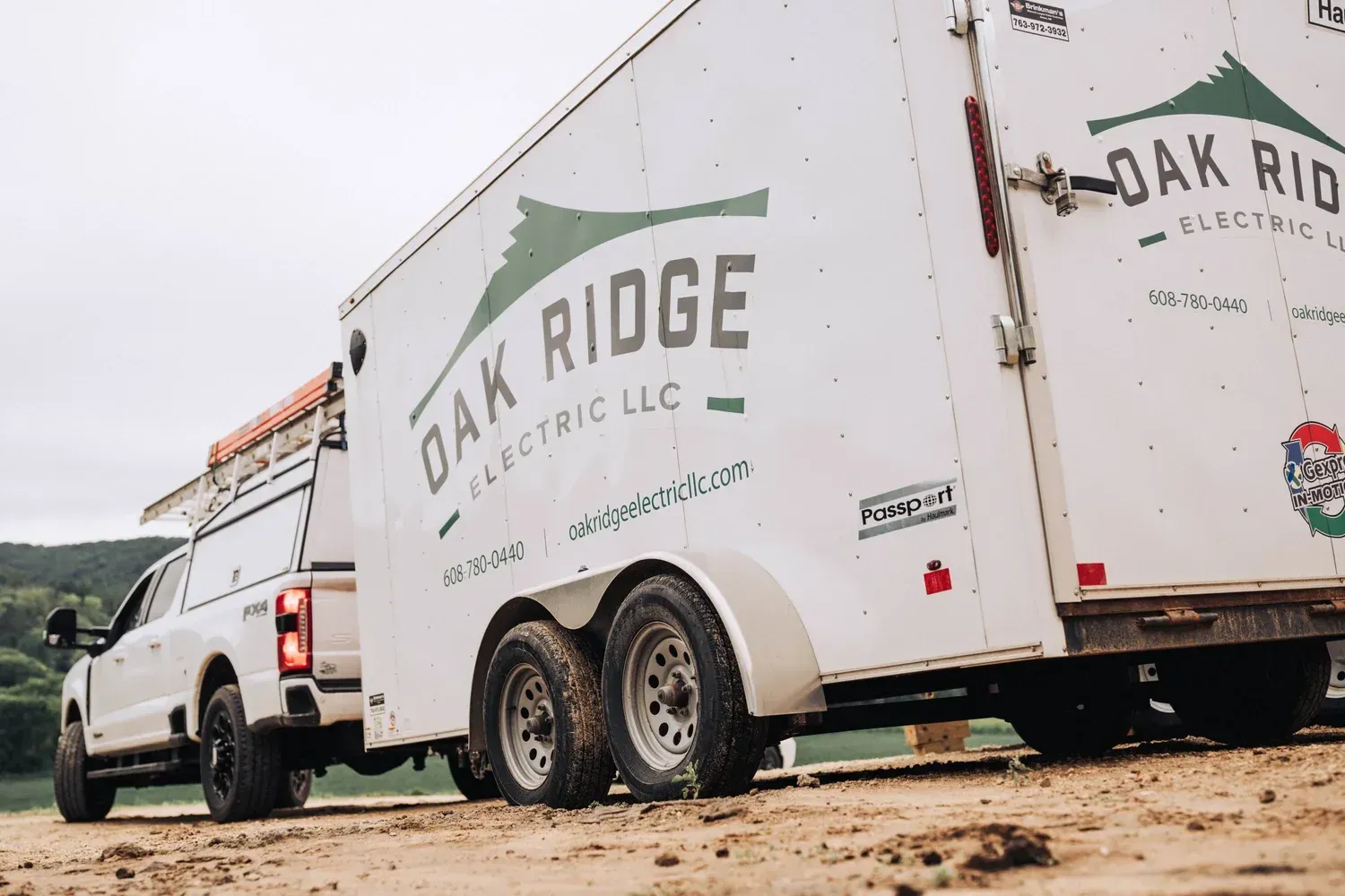 White truck towing a trailer for Oak Ridge Electric LLC on a gravel surface.