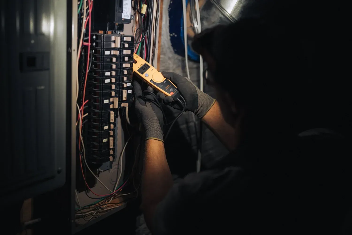 Electrician working on electrical panel, using a multimeter.