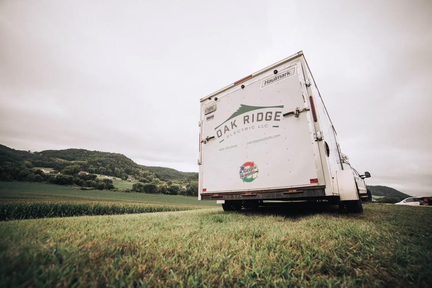 White Oak Ridge truck parked in a green field with a cloudy sky and distant hills.