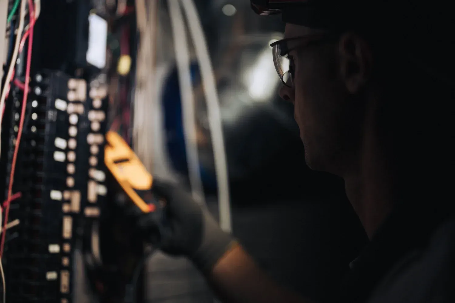 Electrician testing an electrical panel with a multimeter; indoor, dark environment.