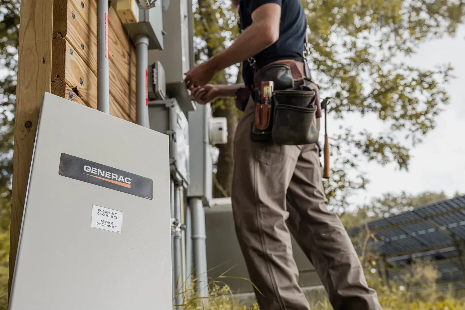 Electrician working on a Generac generator panel outdoors; wearing tool belt.