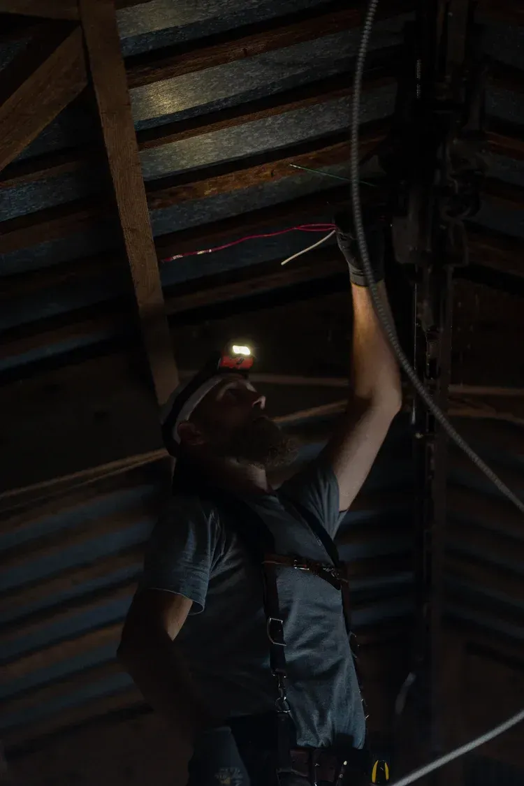 Person with headlamp working on wires in an attic.