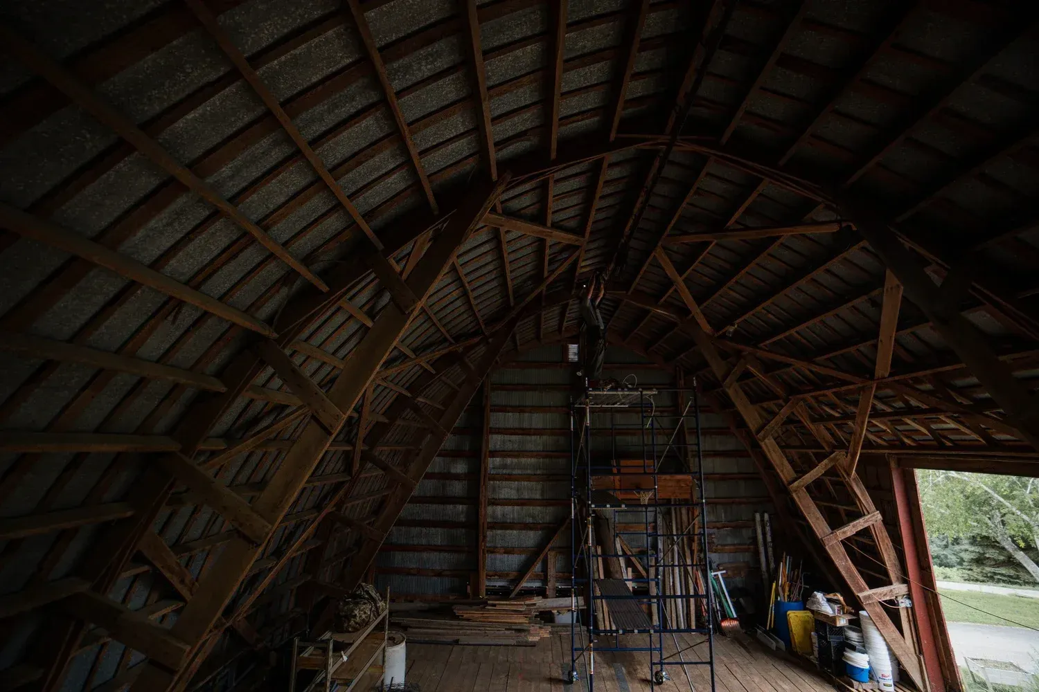Interior view of a wooden barn with an arched roof and various tools and objects.