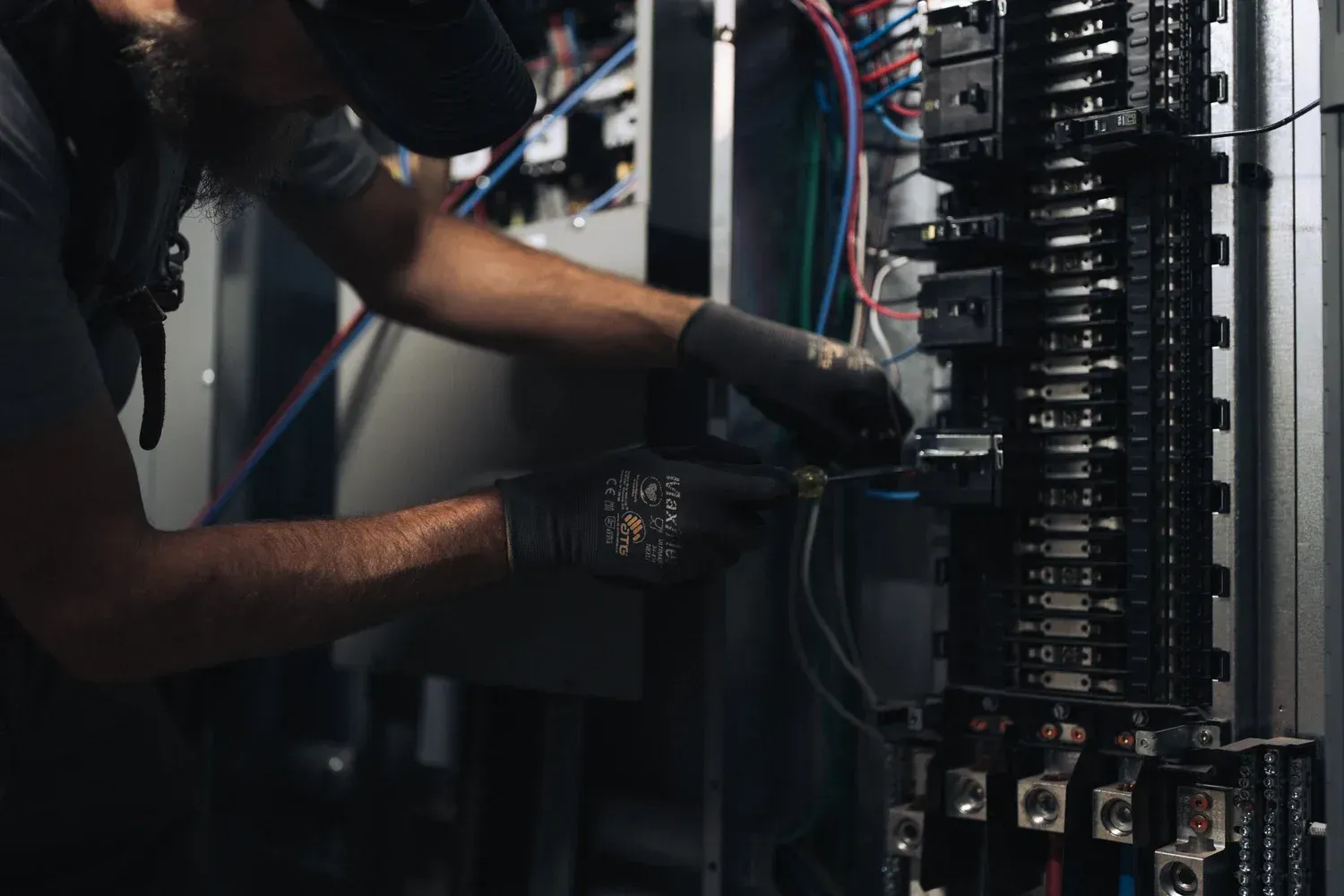 Electrician working on electrical panel, wearing gloves and safety glasses.
