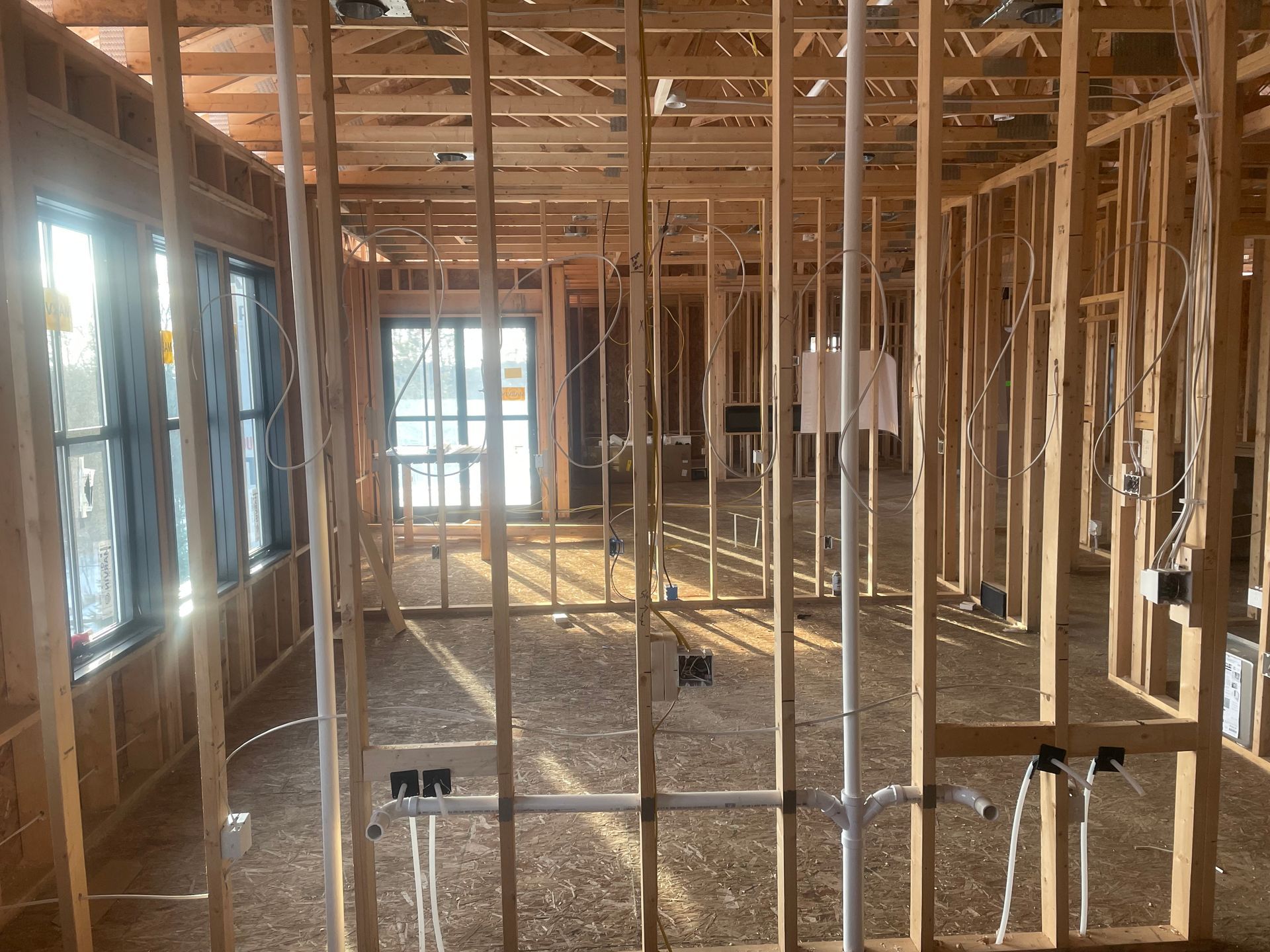 Interior construction site with exposed ceiling, electrical wiring, and white walls.