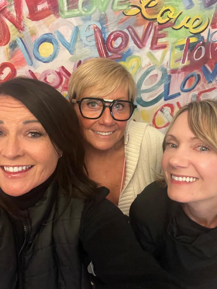 three women are posing for a picture in front of a wall that says love
