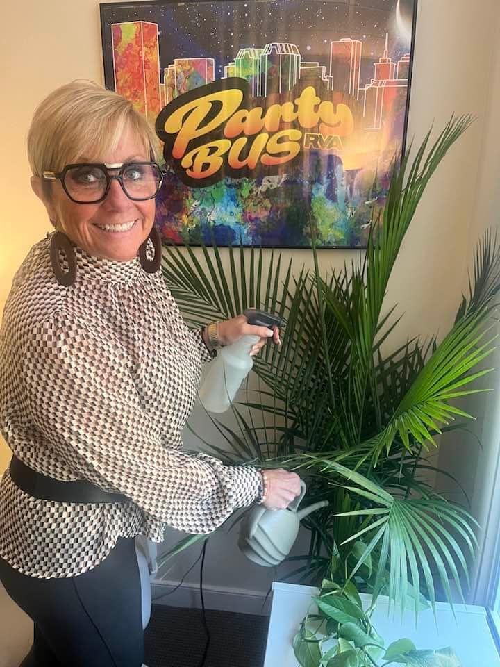 Woman spraying a leafy green plant with a spray bottle, near a 