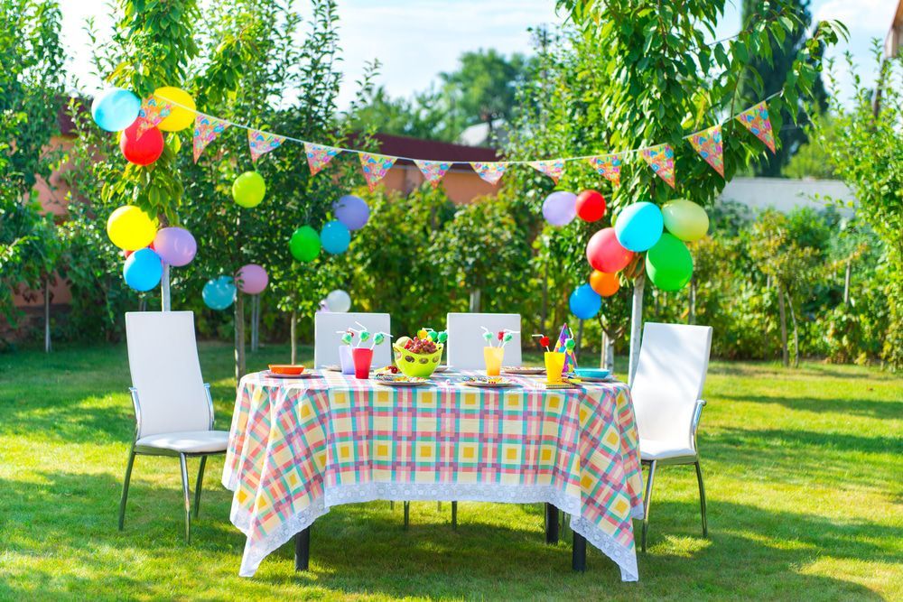Colorful balloons around a table set for a garden party on a sunny lawn