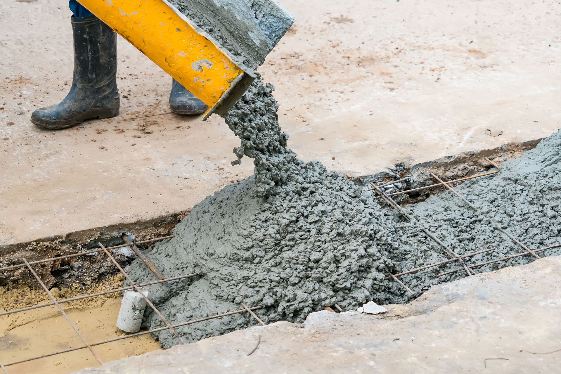 Wet concrete pouring from a yellow mixer chute into a trench on a construction site