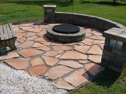 Stone fire pit area with curved brick seating wall and benches in a grassy park.