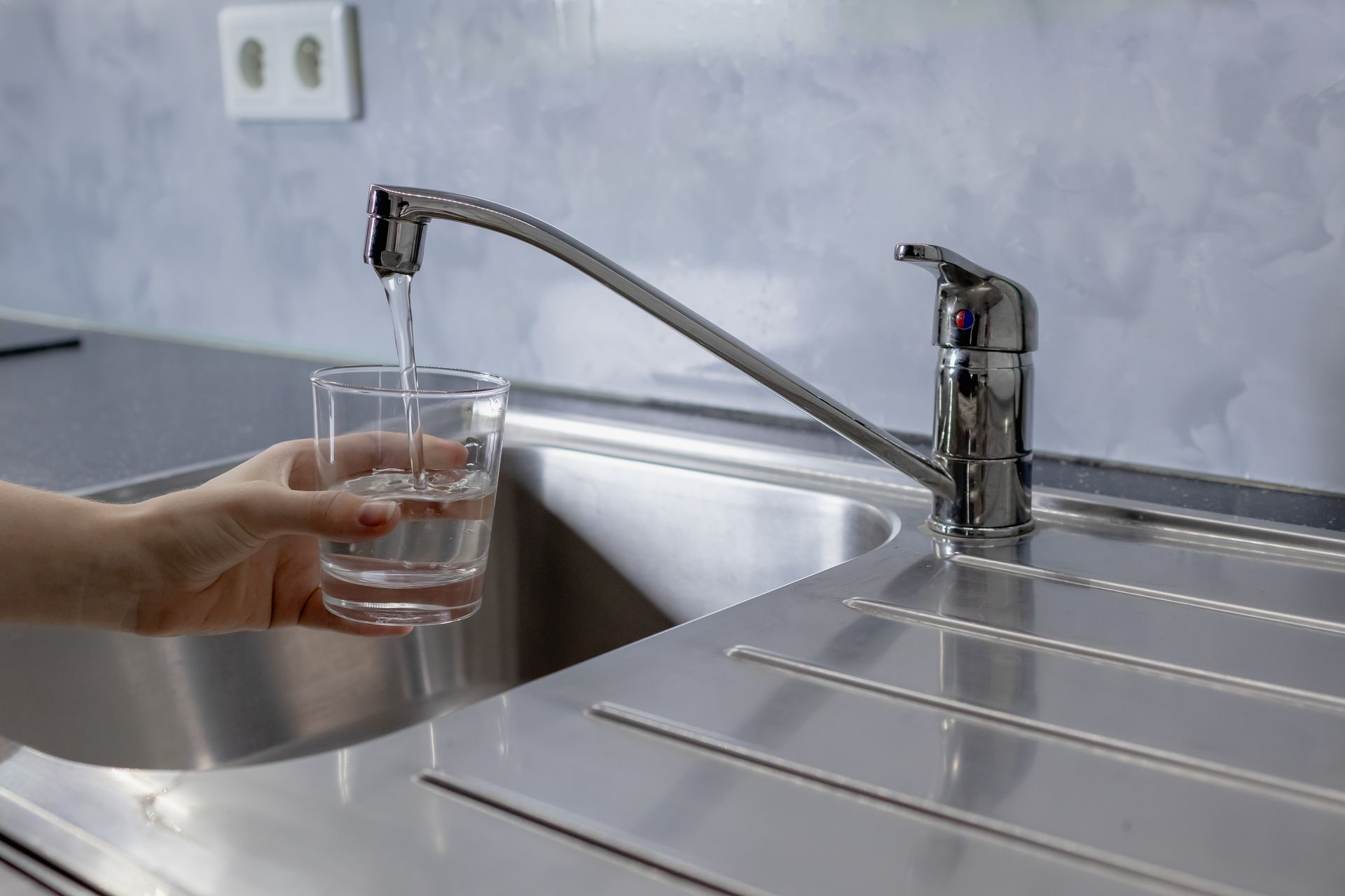 A hand holds a glass under a running kitchen faucet, filling it with water.