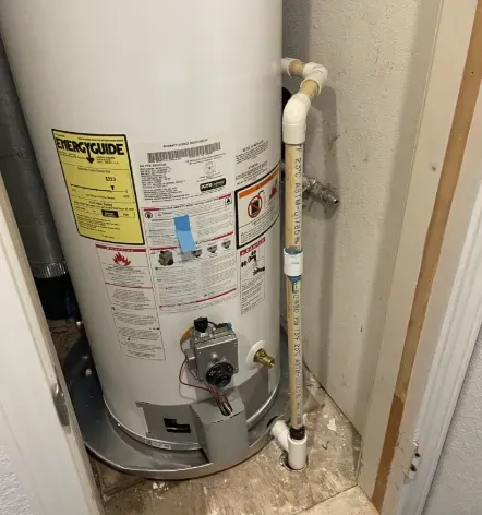 A white residential water heater in a closet, showing the EnergyGuide label, gas control valve, and drain pan.