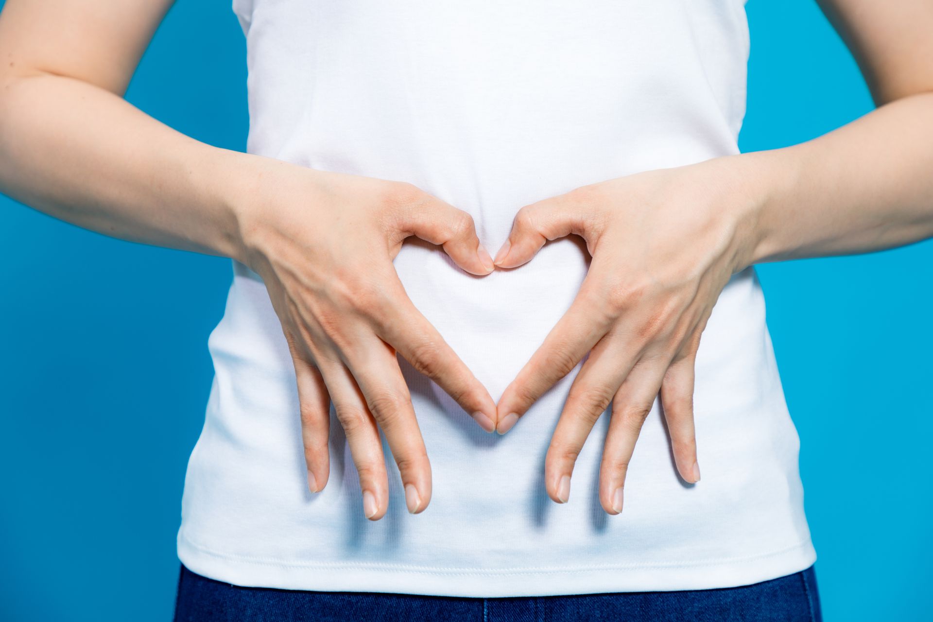 Woman using finger to symbolize the heart shape over her stomach