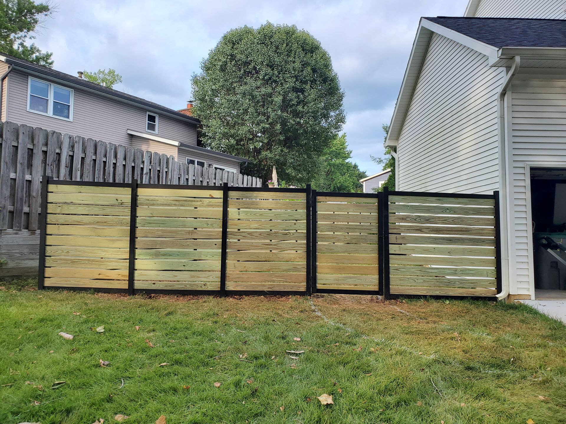 Horizontal wood fence with black framing in a grassy backyard.