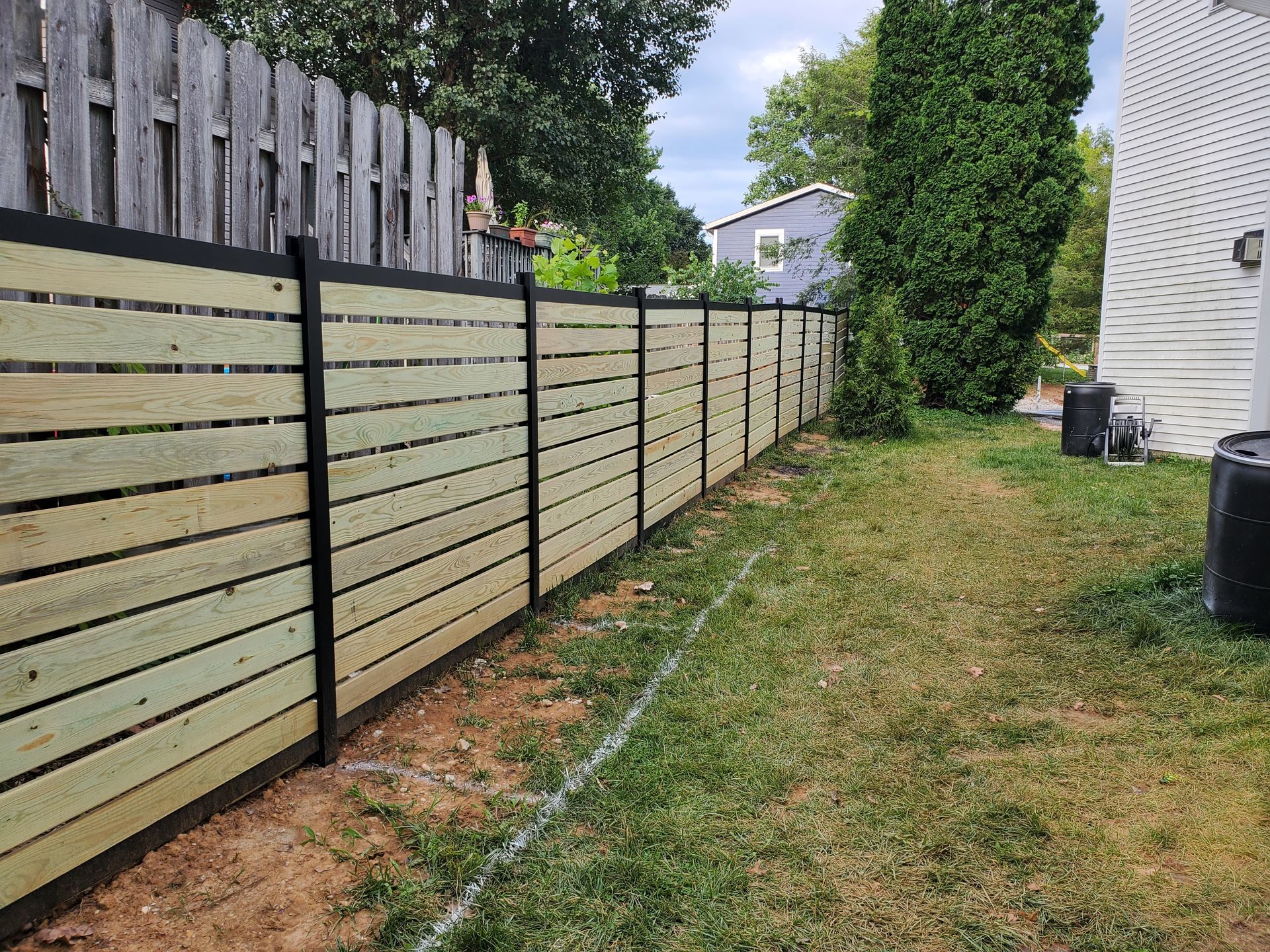 Wooden horizontal slat fence with black posts, bordering a grassy yard.