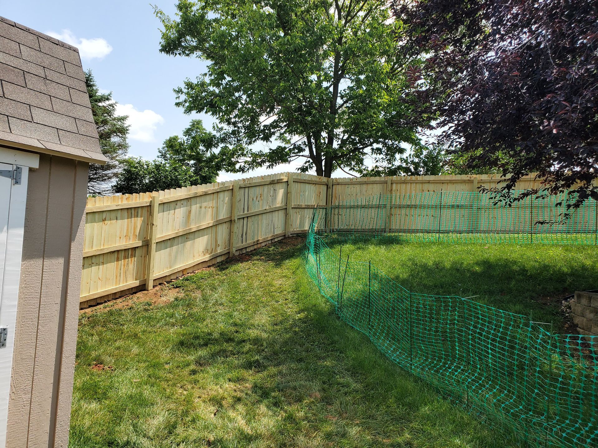 Wooden fence surrounds a grassy yard, partially visible with a green construction barrier.