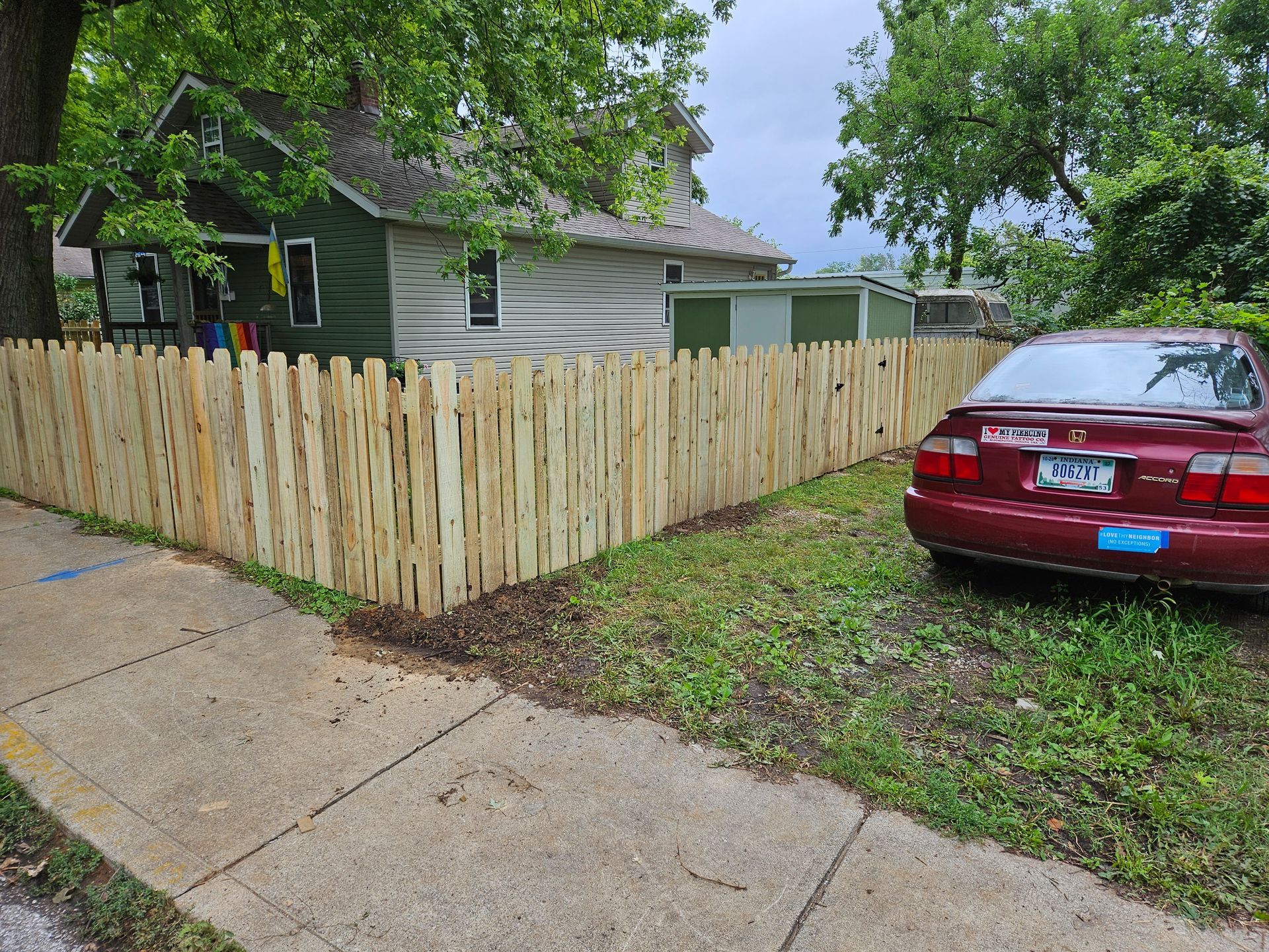 Wooden fence surrounds a house and a red car parked on the grass.