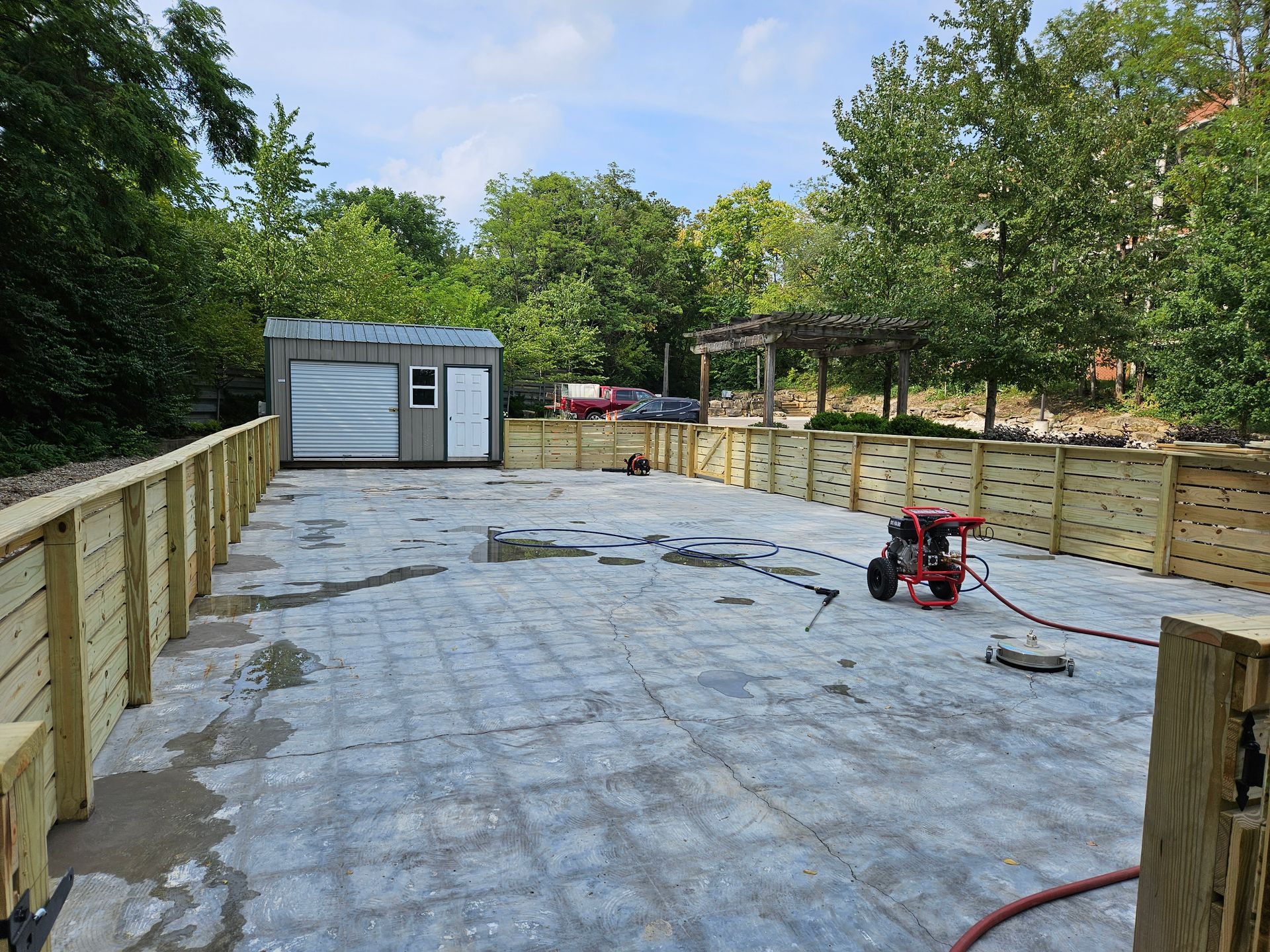 Concrete patio under construction, bordered by wooden fence. A small shed is visible in the background.