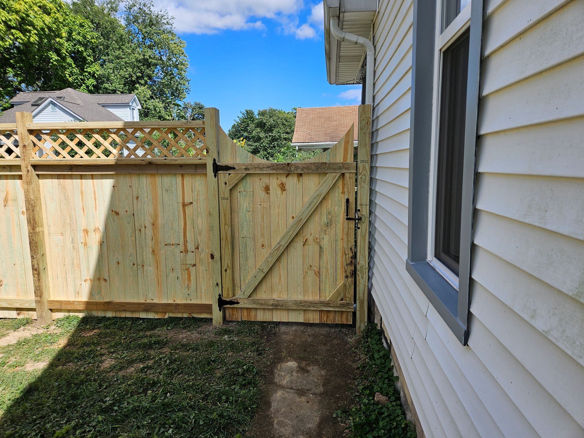 Wooden fence with a gate beside a white house, on a sunny day.
