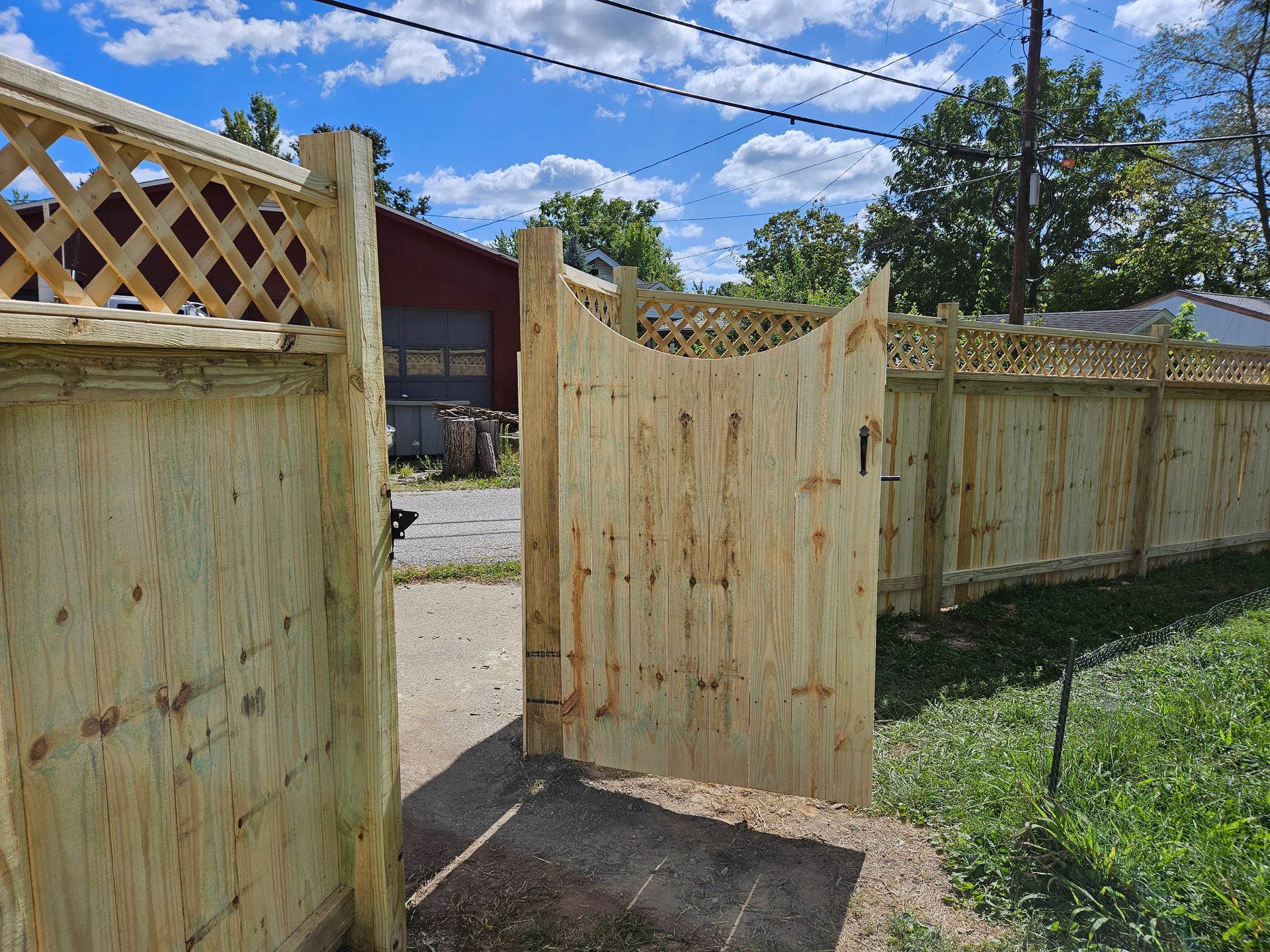 Wooden fence with a gate, in a backyard setting. Lattice-topped fence with a partially open gate, green grass, and blue sky.