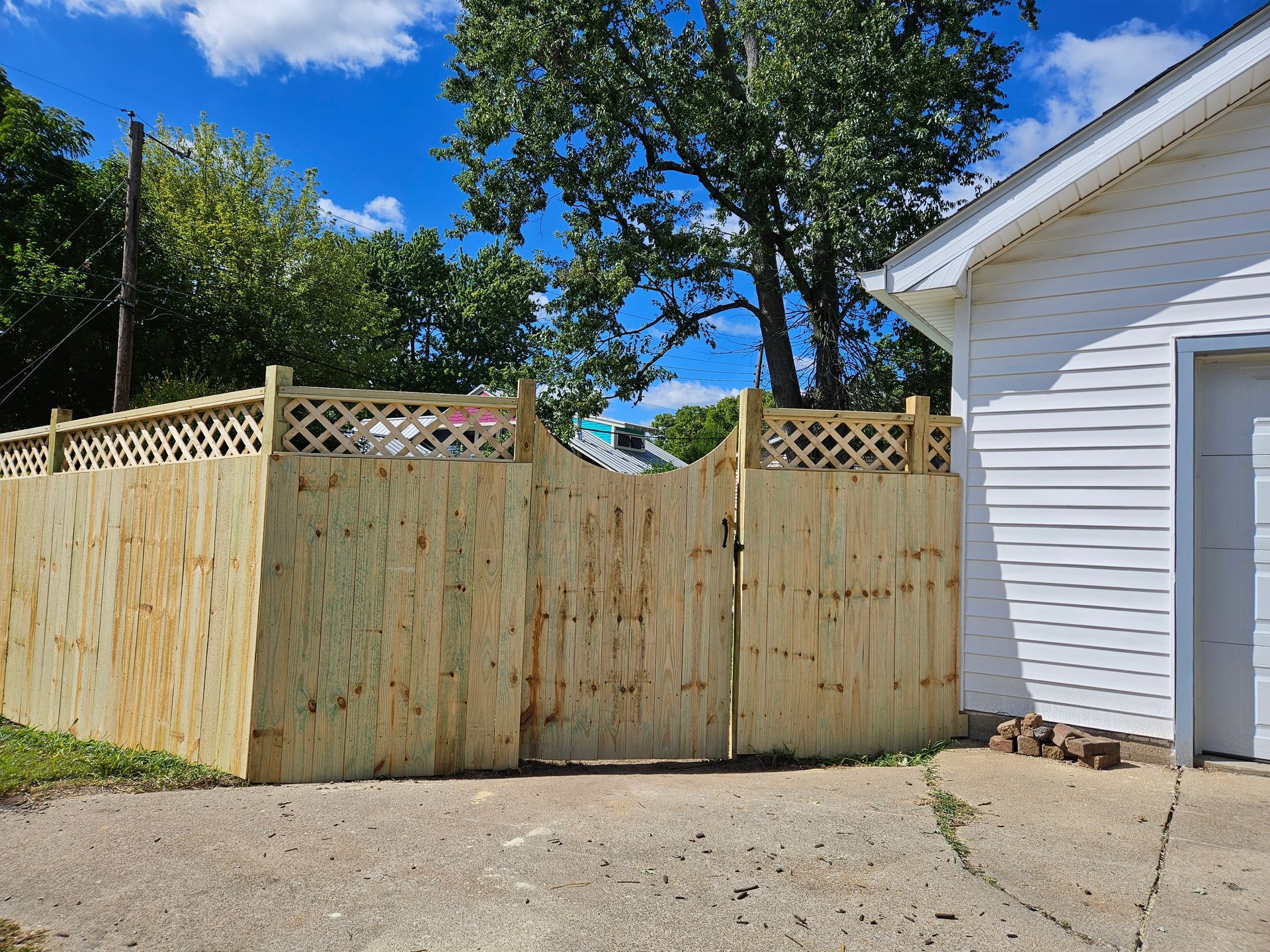 Wooden fence with a gate, next to a white building under a blue sky.