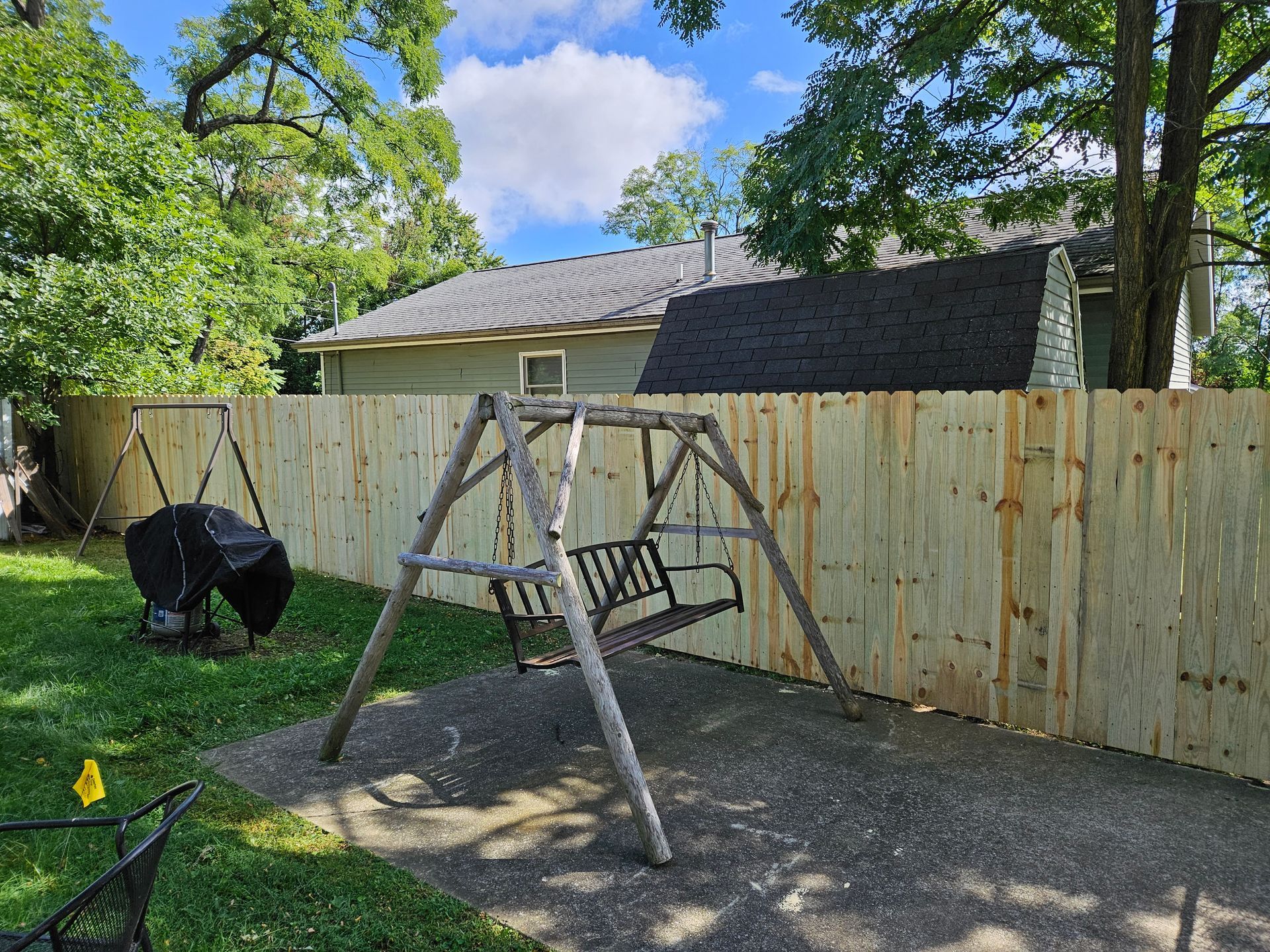 Backyard scene with a wooden swing set, fire pit, and newly built wooden fence.