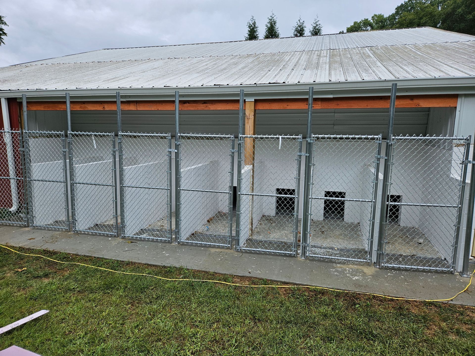 Kennels with chain link fencing and white walls under a building with a metal roof.